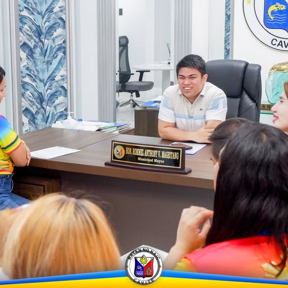 Pulong sa opisina ng alkalde, may nameplate sa mesa at ilang taong nakaupo na nakaharap sa lamesa