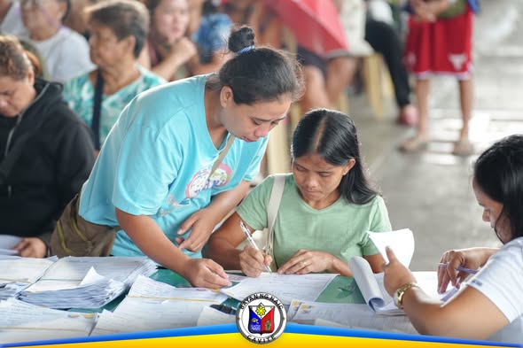 Mga tao habang nagsusulat ng mga papeles sa mesa ng pamamahagi ng tulong sa Naic Town Plaza