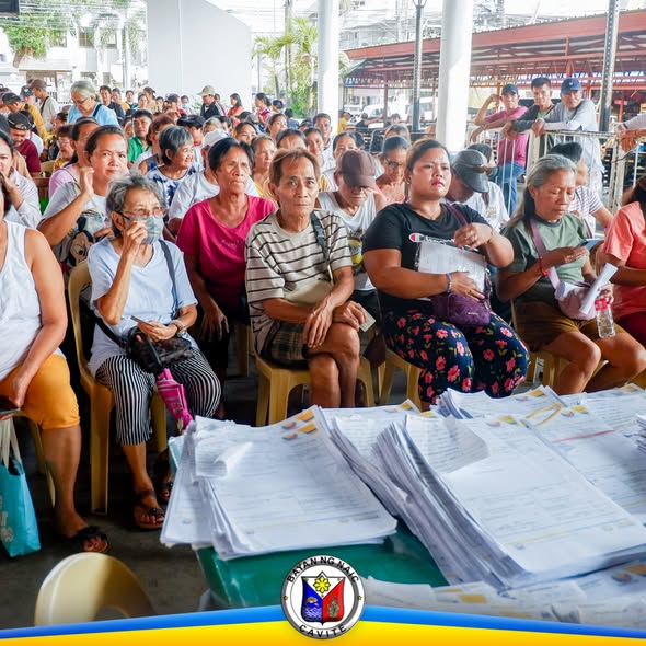 Mga residente na nakaupo sa covered area habang naghihintay ng burial assistance sa Naic Town Plaza
