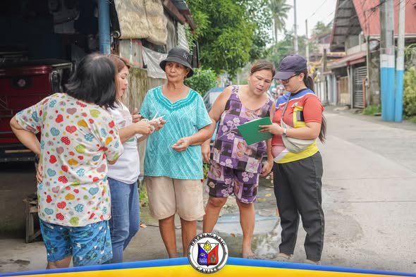 Mga kababaihan sa kalye ng Barangay Sapa habang tumatanggap ng impormasyon at papeles mula sa health worker