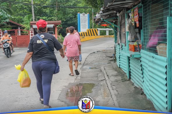 Mga BHW na naglalakad sa makitid na kalsada sa Barangay Sapa habang may dalang plastic na supot