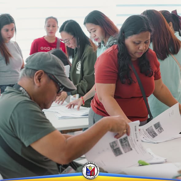 Mga tao habang sinusuri ang mga papel sa mesa sa loob ng gusali para sa SLP Project Proposal sa Naic