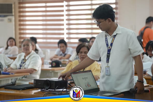 Staff na nagpapakita ng presentasyon sa laptop habang nanonood ang mga kalahok sa pulong ng Performance Management Team
