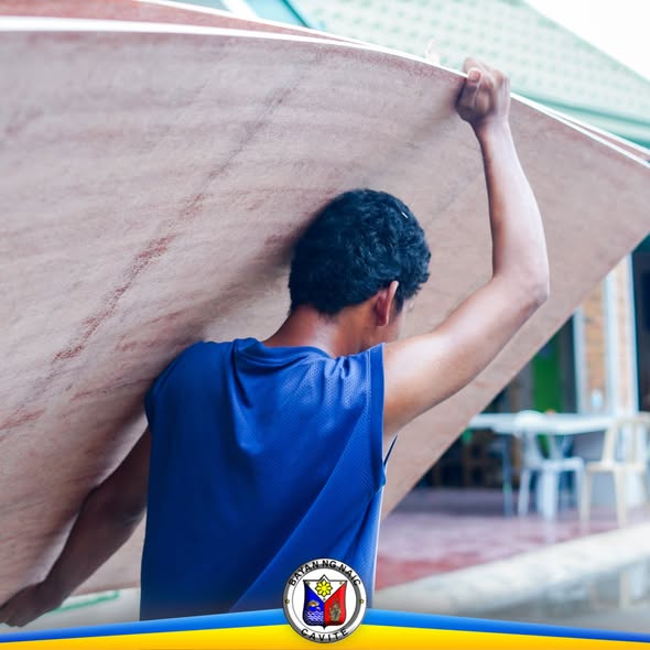 Taong nagbubuhat ng plywood sa balikat, bahagi ng pamamahagi ng kagamitan sa mga paaralan