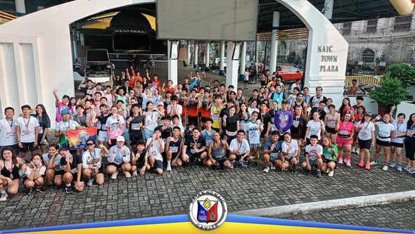 Grupo ng mga kalahok sa HAKBANG Fun Run 2026 na nagpose sa harap ng Naic Town Plaza arch