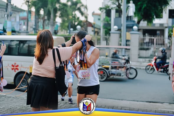 Dalawang kalahok sa HAKBANG Fun Run 2026 habang may isinusuot na medalya sa Naic Town Plaza