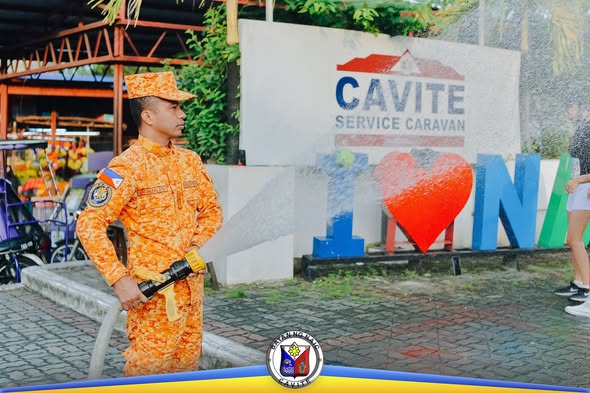 Naka-unipormeng tauhan na nakatayo sa harap ng Cavite Service Caravan sign sa Naic Town Plaza