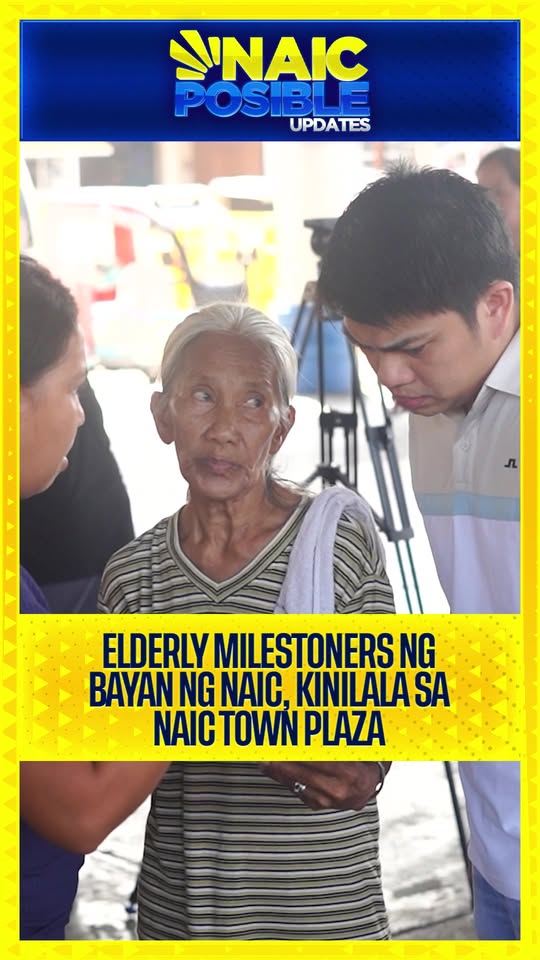 Matandang babae habang kausap ng isang lalaki at babae sa labas, may tripod ng kamera sa likuran