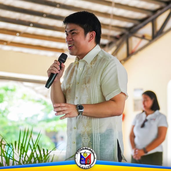 Lalaking nagsasalita gamit ang mikropono sa covered court habang nagbibigay ng mensahe sa pamamahagi ng school supplies
