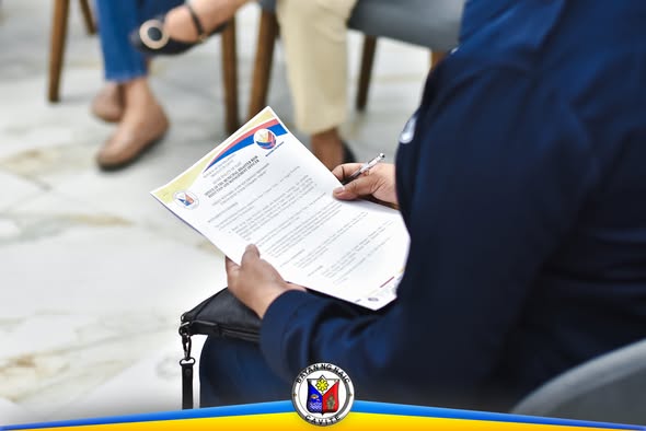 Taong naka-uniporme ng asul na nagbabasa ng dokumento habang may hawak na ballpen sa pulong ng PDRA