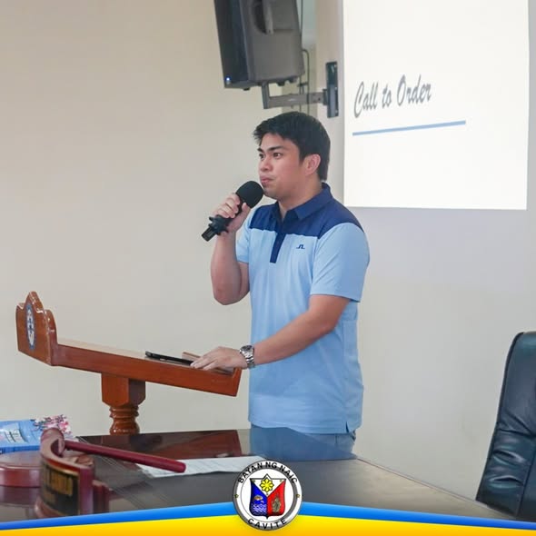 Lalaking nagsasalita gamit ang mikropono sa podium, may slide na "Call to Order" sa likod, sa ABC Hall, Naic