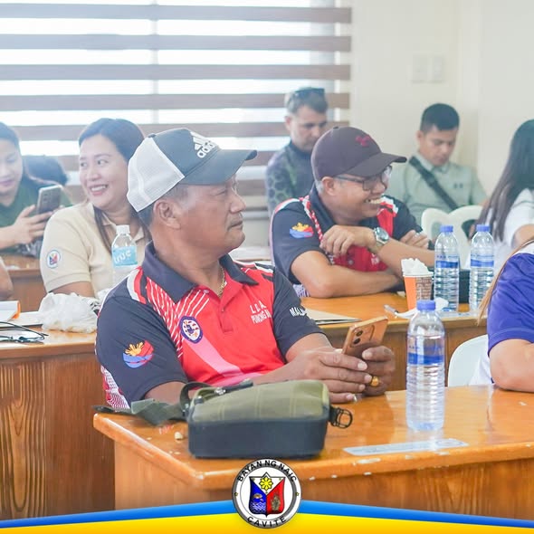 Mga kalahok sa Liga ng mga Barangay na nakaupo sa ABC Hall, Naic, habang may hawak na cellphone ang ilan