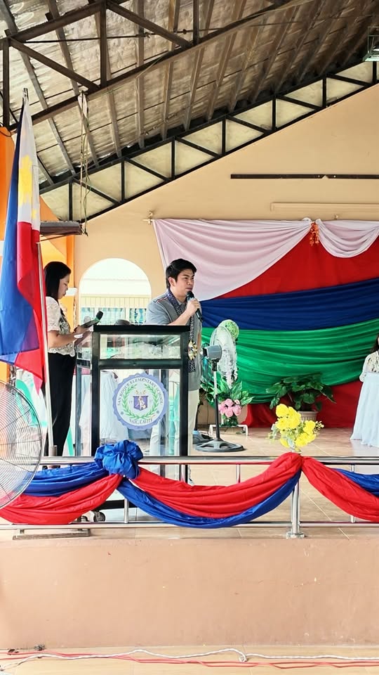 Isang opisyal na nagsasalita sa podium sa entablado ng pagtatapos ng ALS sa San Roque Elementary School, Naic