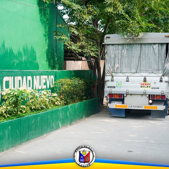 Trak na may tarpaulin na nakaparada sa tabi ng berdeng pader na may pangalang Ciudad Nuevo sa Naic, Cavite