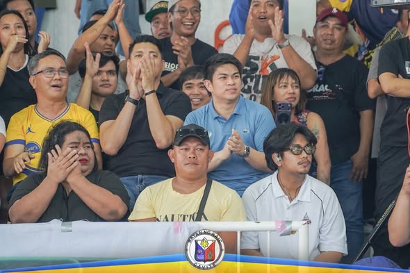 Mga manonood na pumapalakpak at nagchi-cheer sa bleachers habang nanonood ng laro ng Team Naic Posible