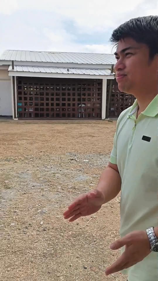 Lalaking nagpapaliwanag sa lupang lote sa harap ng gusali ng Pasinaya Prime South, Naic