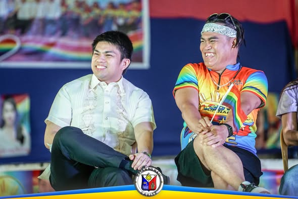 Dalawang lalaking nakangiti habang nakaupo sa entablado sa Pride Month Celebration sa Naic Town Plaza