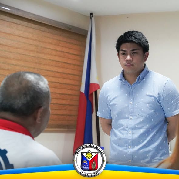 Pulong sa opisina ng Naic habang nag-uusap ang dalawang lalaki sa harap ng watawat ng Pilipinas
