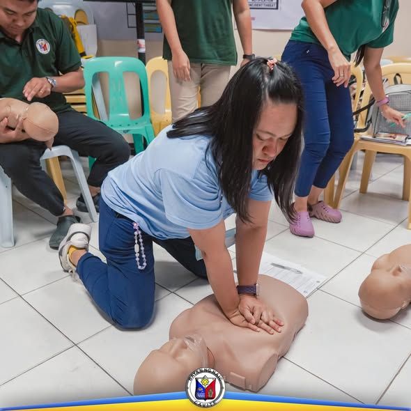 Pagsasanay sa CPR: babaeng nagsasagawa ng chest compression sa manikin habang nanonood ang mga kalahok sa Naic