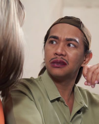 Lalaking naka-olive na polo at sumbrero, nakatingin sa gilid habang may kausap sa harap