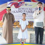 Tatlong bata sa entablado habang nagsasalita ang isa sa Buwan ng Wikang Pambansa 2025 sa Naic