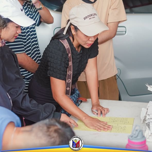 Babaeng pumipirma ng yellow na form sa mesa habang nakapila ang mga tao sa PhilHealth caravan sa Naic