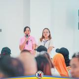 Babaeng nagsasalita gamit ang mikropono sa harap ng mga dumalo sa pagpupulong ng Local Development Council