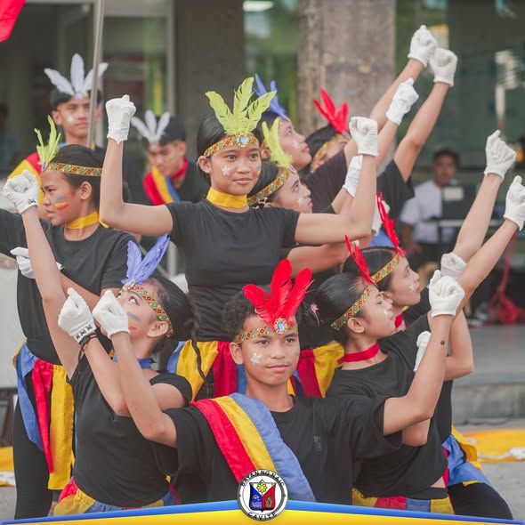 Mga mag-aaral na nagsasayaw ng interpretasyon ng Himno ng Naic sa flag raising ceremony, may balahibo at pintura sa mukha