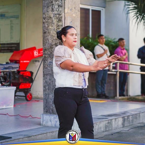 Babaeng nagsasalita at nagpapaliwanag sa flag-raising ceremony ng Lokal na Pamahalaan ng Naic sa labas ng gusali