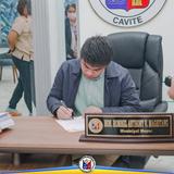 Isang opisyal na pumipirma ng dokumento sa mesa sa loob ng opisina ng Naic, Cavite