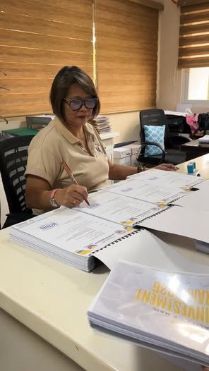 Isang babaeng pumipirma sa mga dokumento ng AIP sa opisina ng Naic