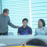 Mga kalahok na masayang nag-uusap sa mesa habang may lalaking nakatayo at nakahawak sa balikat ng isa sa conference