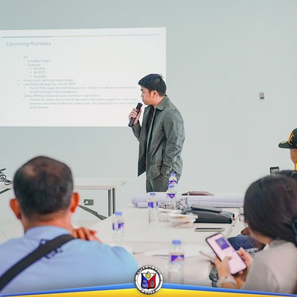 Lalaking nagsasalita sa mikropono sa harap ng screen na may 'Upcoming Activities' sa pulong ng board
