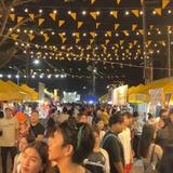 Mga tao sa Naic Posible Food Bazaar Season 1 sa gabi, may ilaw at bandila at mga food stall.