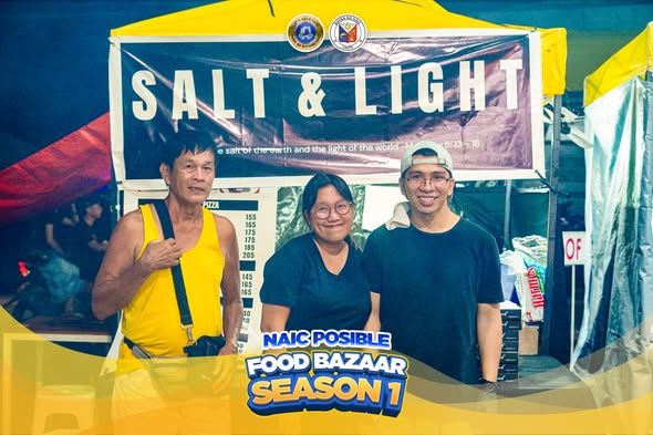 Tatlong tao sa harap ng food stall na may banner na "SALT & LIGHT" sa Naic Posible Food Bazaar