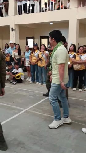 Isang lalaking naka-polong berde habang naglalakad sa court, pinanonood ng mga estudyante sa Sport Fest ng CvSU Naic
