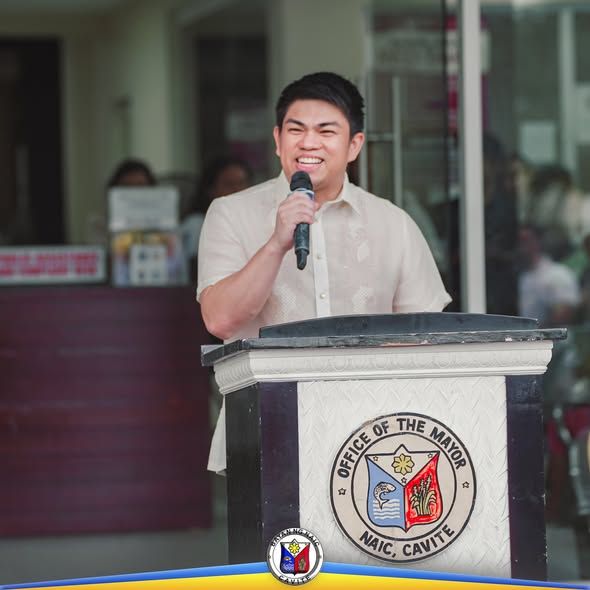 Lalaking nagsasalita sa mikropono sa podium ng Office of the Mayor, Naic, Cavite, sa flag raising ceremony